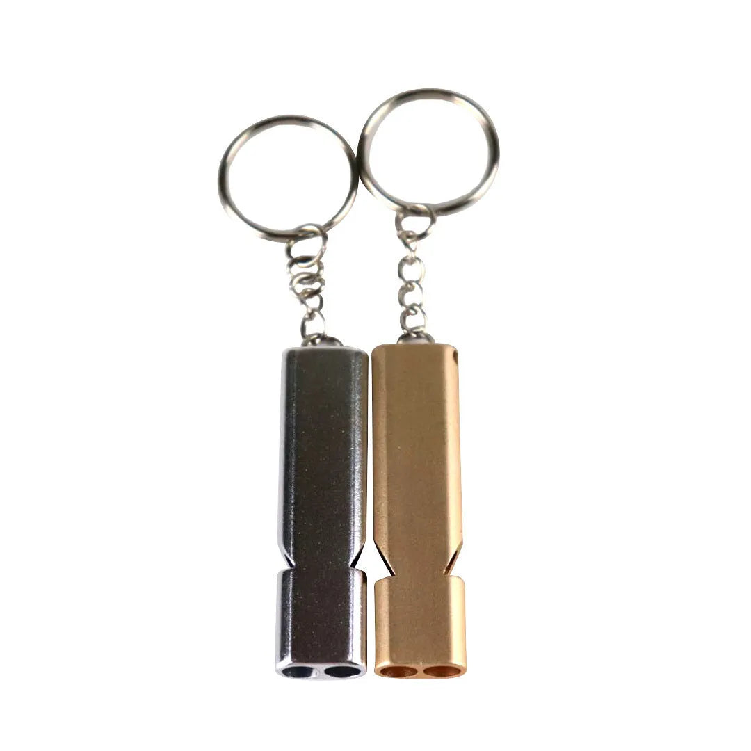 A silver or gold coloured aluminium alloy survival whistle with two holes on a grey background.