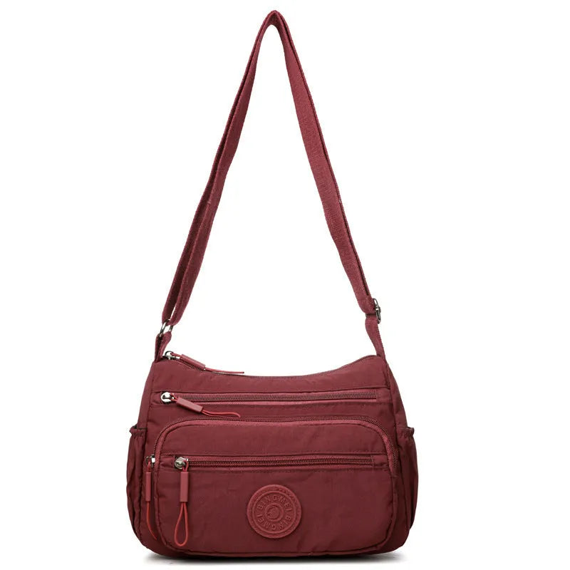 Soft nylon crossbody bag in black, grey, or red with a single shoulder strap and water-repellent finish.