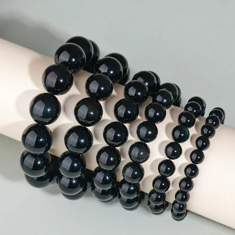 Hand-woven round obsidian crystal bracelet in black, silver, and rainbow eye colours on a neutral background.