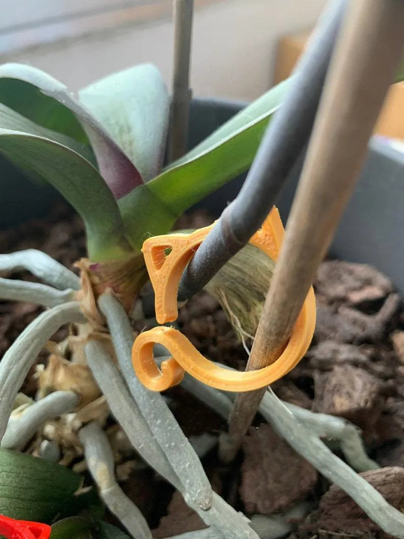 A small red cat-shaped plastic clip for holding plant stems, shown next to a green leaf.