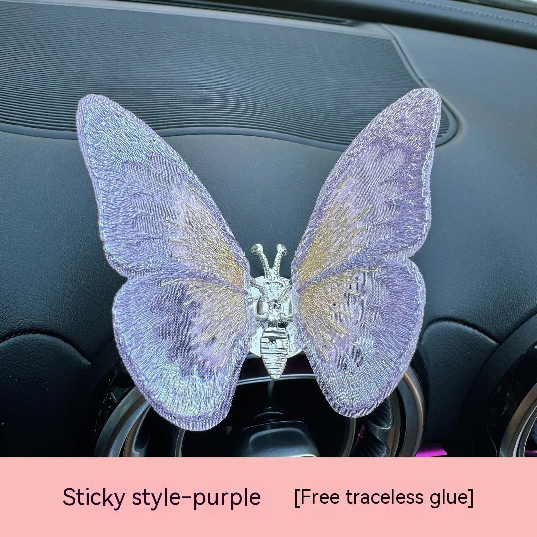 Soft fabric embroidered butterfly car air vent decoration in multiple colour options on a centre console.