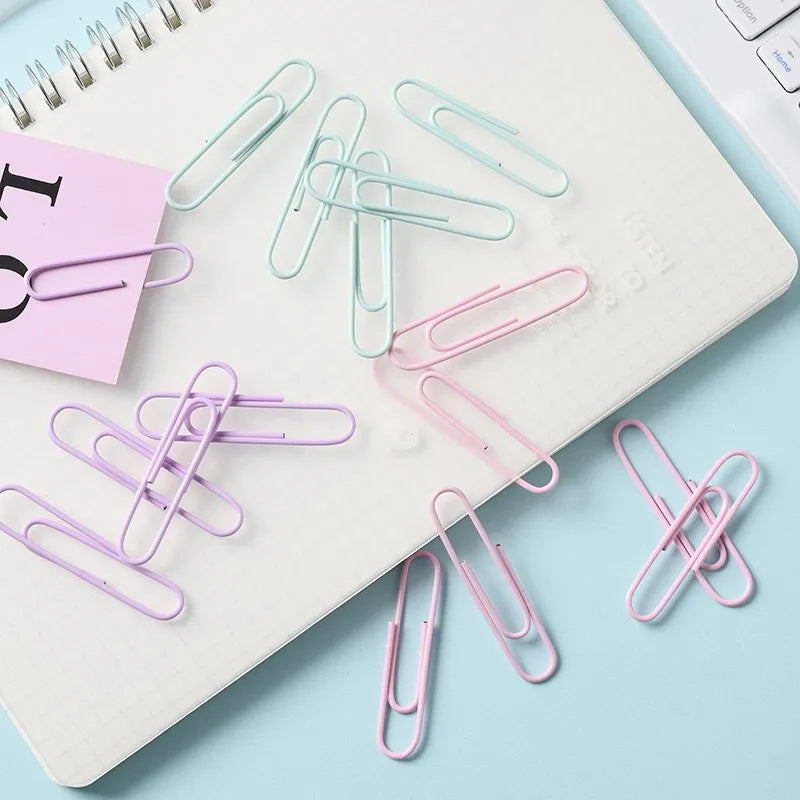 Macaron-color paper clips in pastel shades including pink, green, and purple on a white desk