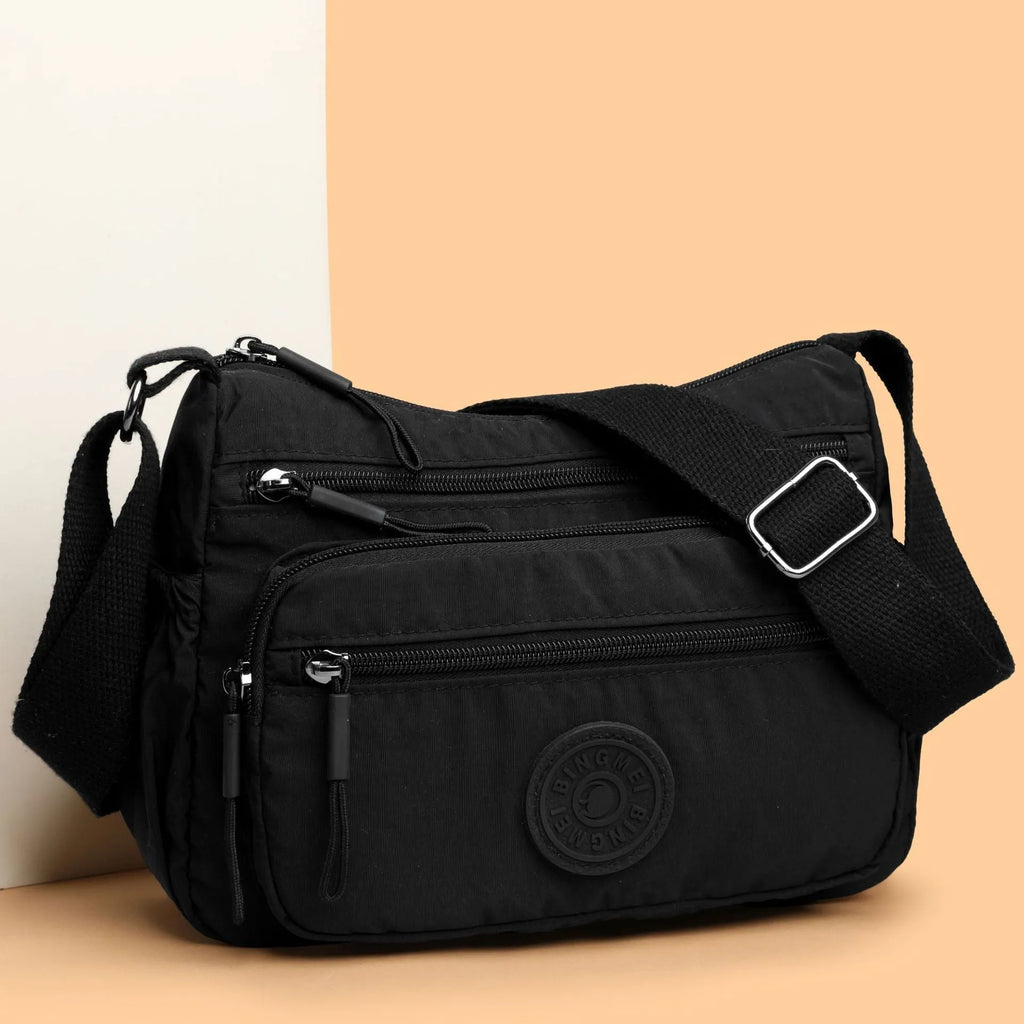 Soft nylon crossbody bag in black, grey, or red with a single shoulder strap and water-repellent finish.