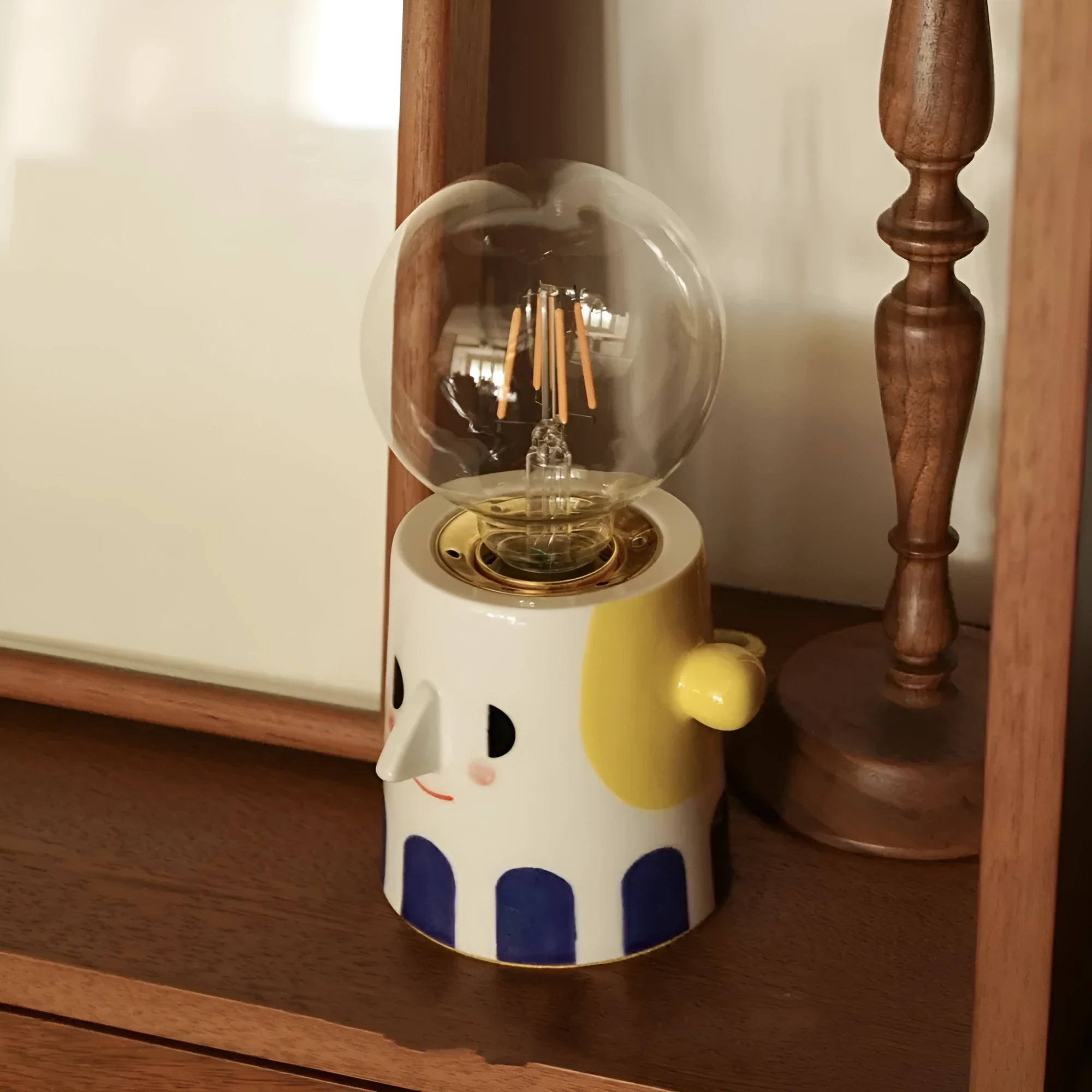 Handmade ceramic ball headlight lamp with a white glaze and integrated UK plug on a wooden table.