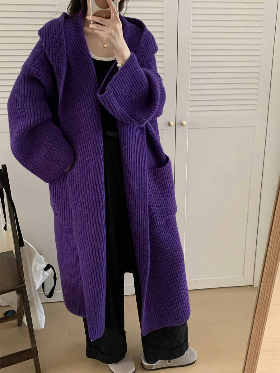 A woman wearing a long, loose, hooded cardigan coat in a neutral colour, showing its oversized fit and length.