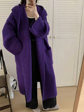 A woman wearing a long, loose, hooded cardigan coat in a neutral colour, showing its oversized fit and length.