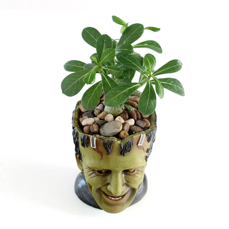 Green Frankenstein monster resin flower pot on a desk with a small succulent plant inside