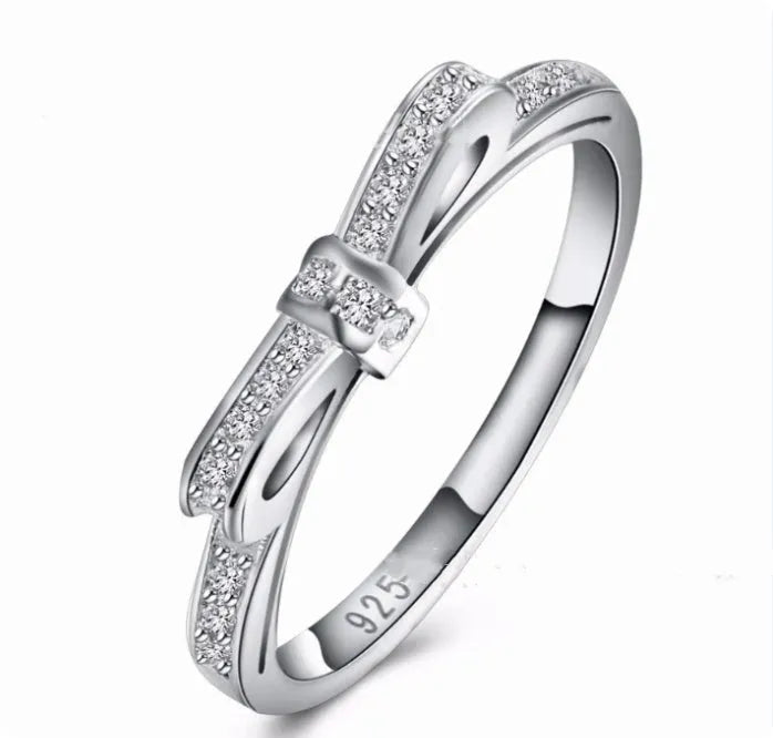 Silver coloured ring with a detailed three-dimensional bow design set with sparkling zircon crystals on a finger.