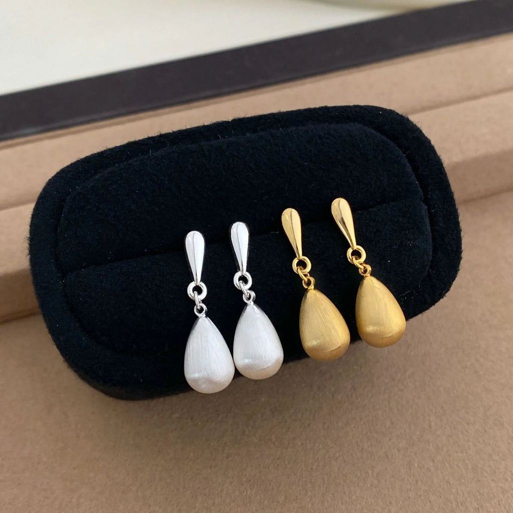 Close-up of wire drawing drop pendant ear clips in geometric teardrop shape, copper with gold electroplated finish