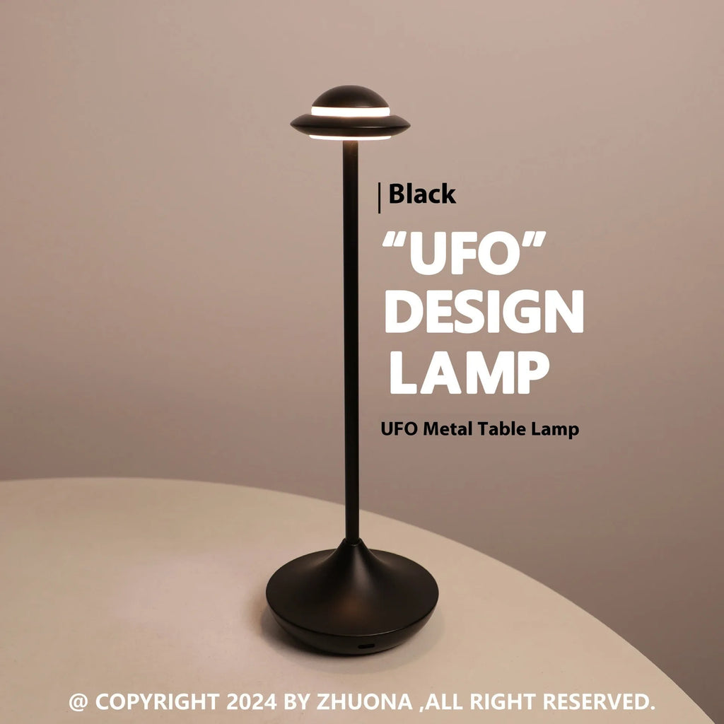 UFO-shaped metal desk lamp with saucer design in grey finish on a wooden table, demonstrating cordless use.