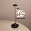 UFO-shaped metal desk lamp with saucer design in grey finish on a wooden table, demonstrating cordless use.