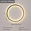 Minimalist black ring wall lamp with acrylic shade mounted on a bedroom wall