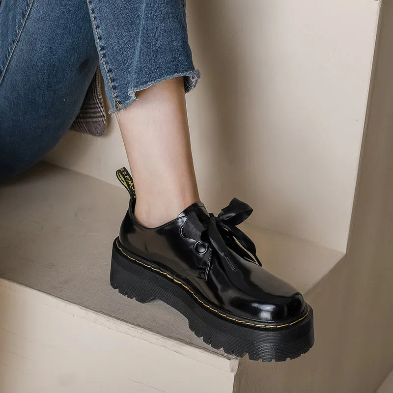 Women's black leather shoes with a thick sole, cross strap, and lace-up closure.
