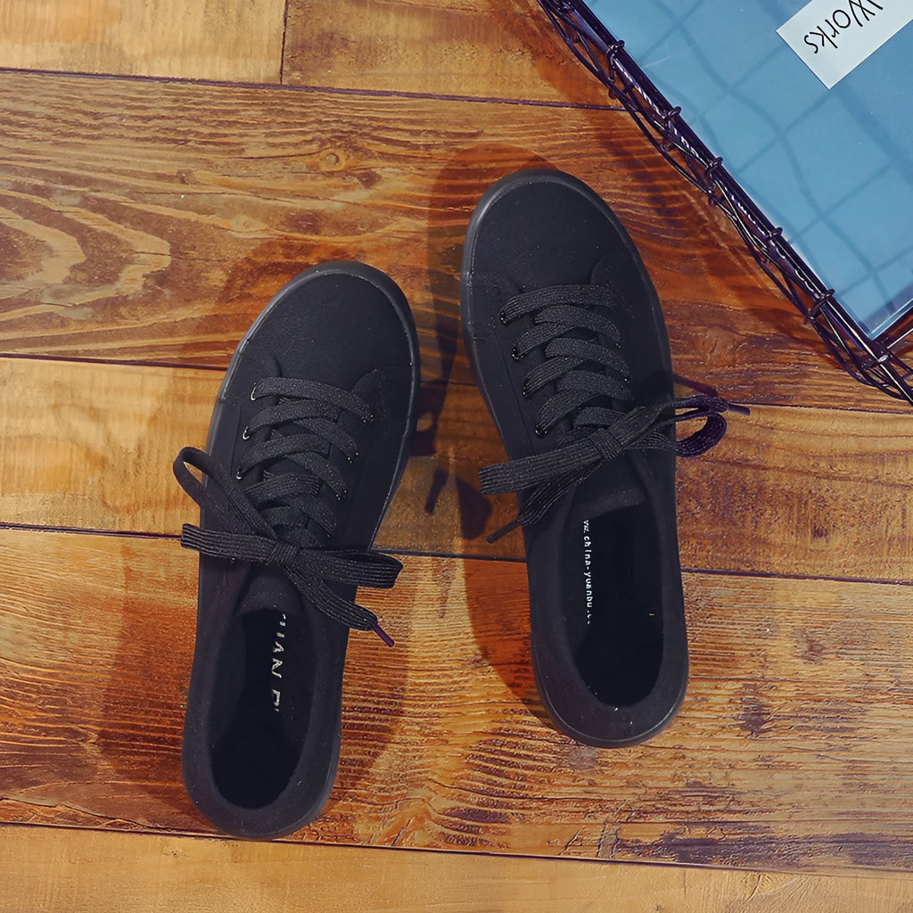 All black women's low-top canvas flat shoes with flat rubber sole and lace-up front.