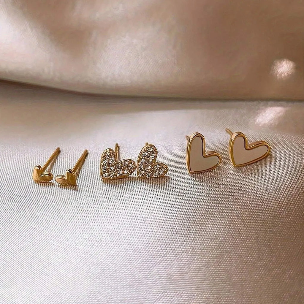 Set of three pairs of women's heart-shaped alloy earrings in gold, black, white, and pink.
