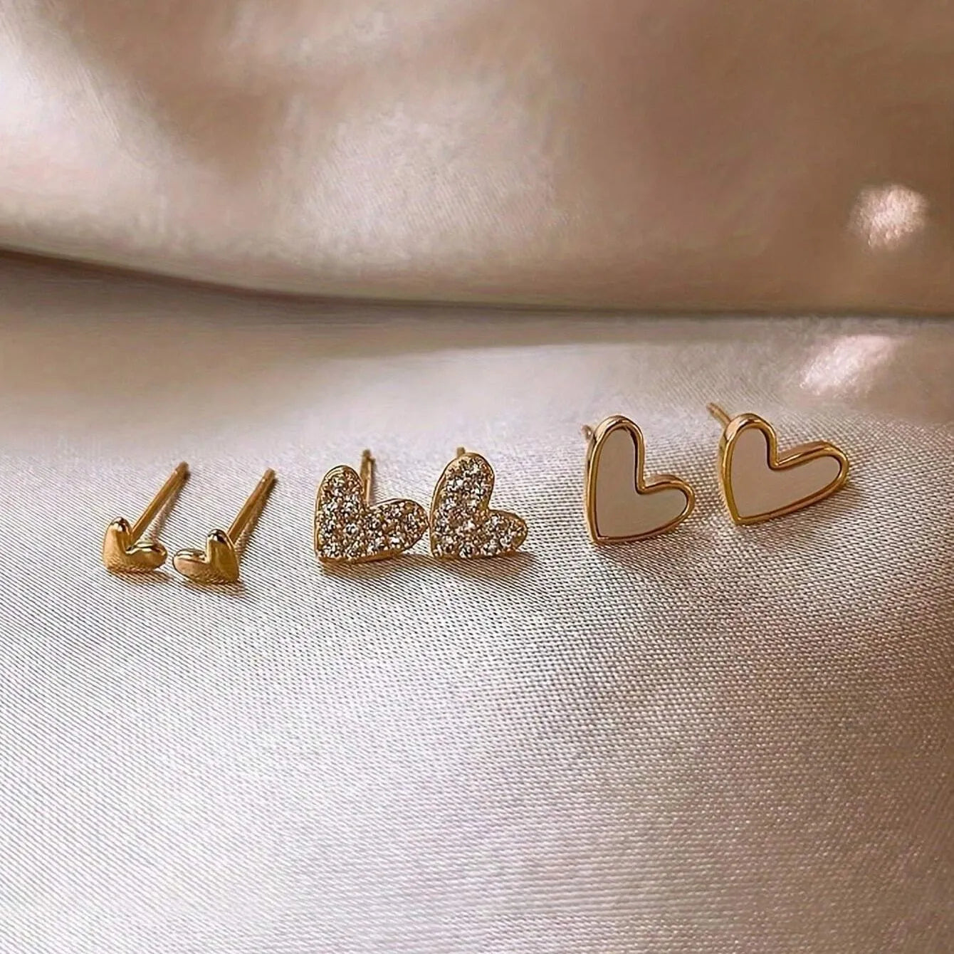 Set of three pairs of women's heart-shaped alloy earrings in gold, black, white, and pink.