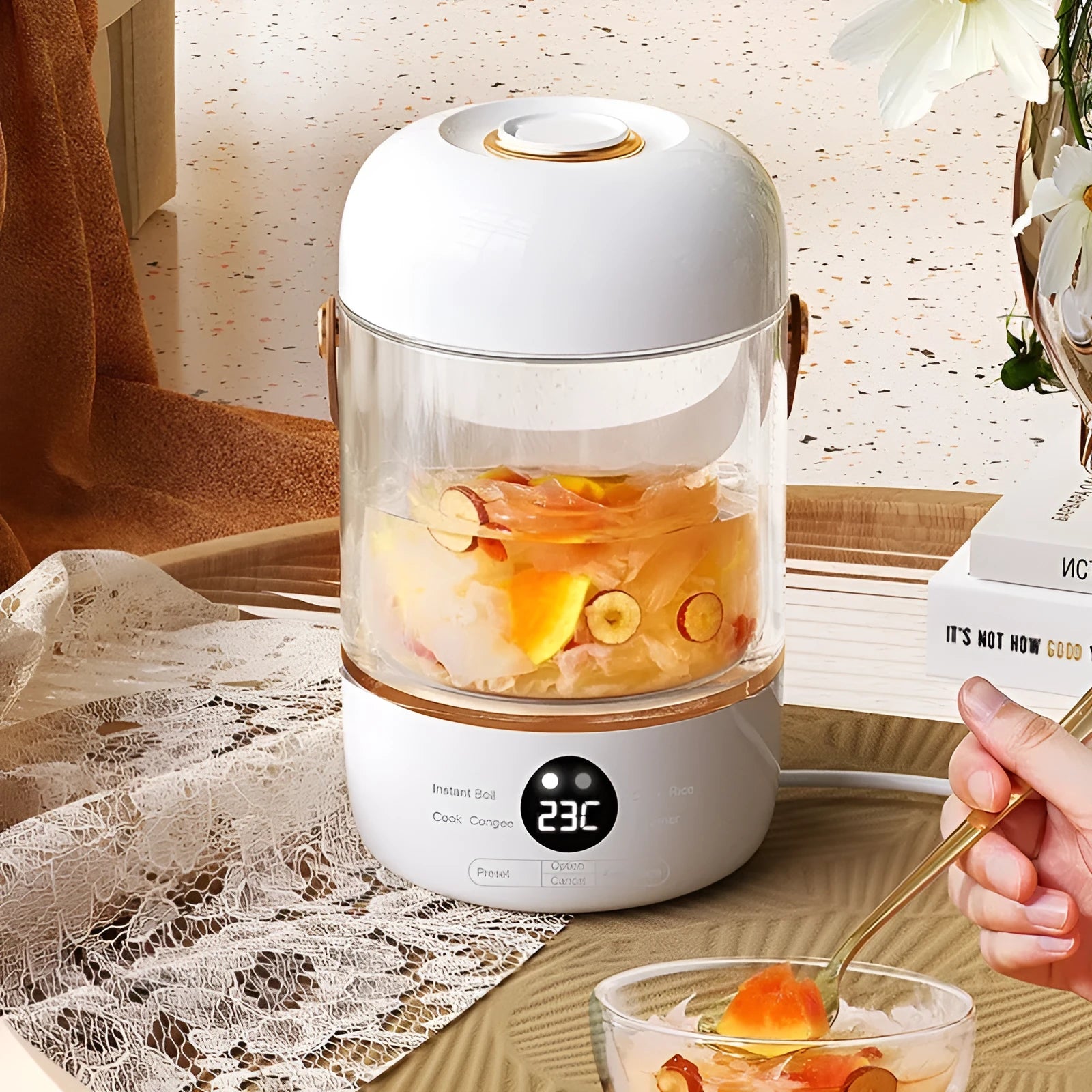 Personal portable electric stew cooker with transparent glass pot and fibreglass body on a desk.