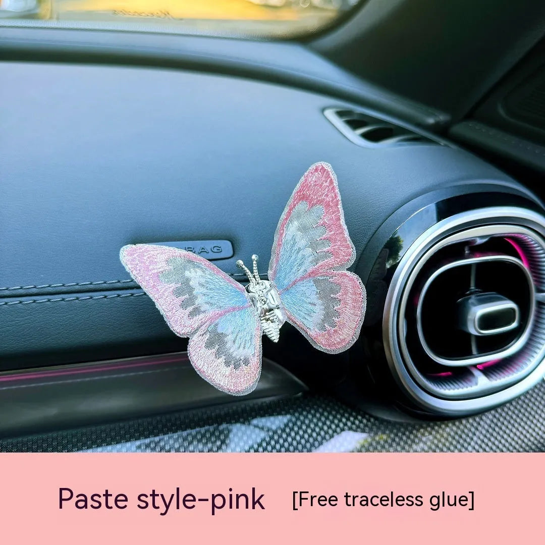 Soft fabric embroidered butterfly car air vent decoration in multiple colour options on a centre console.