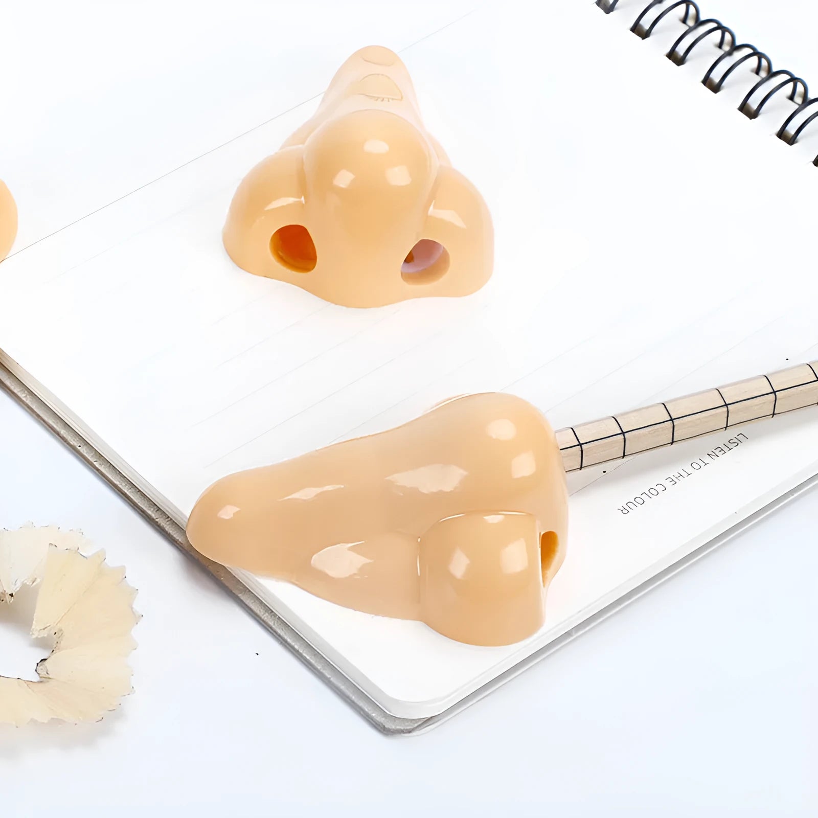 Flesh-coloured plastic pencil sharpener with large nostril and geometric shape on a white background.