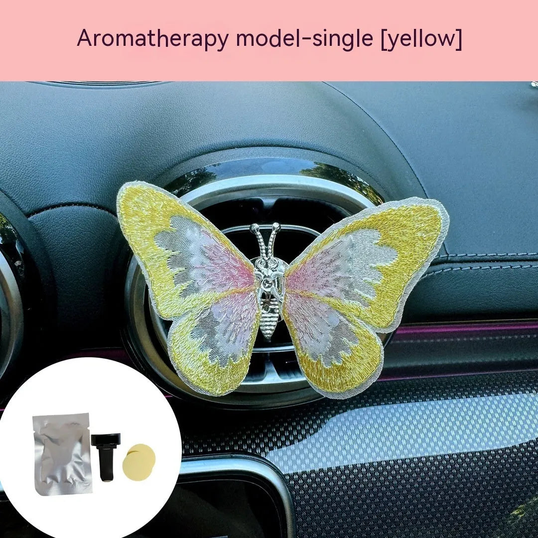 Soft fabric embroidered butterfly car air vent decoration in multiple colour options on a centre console.