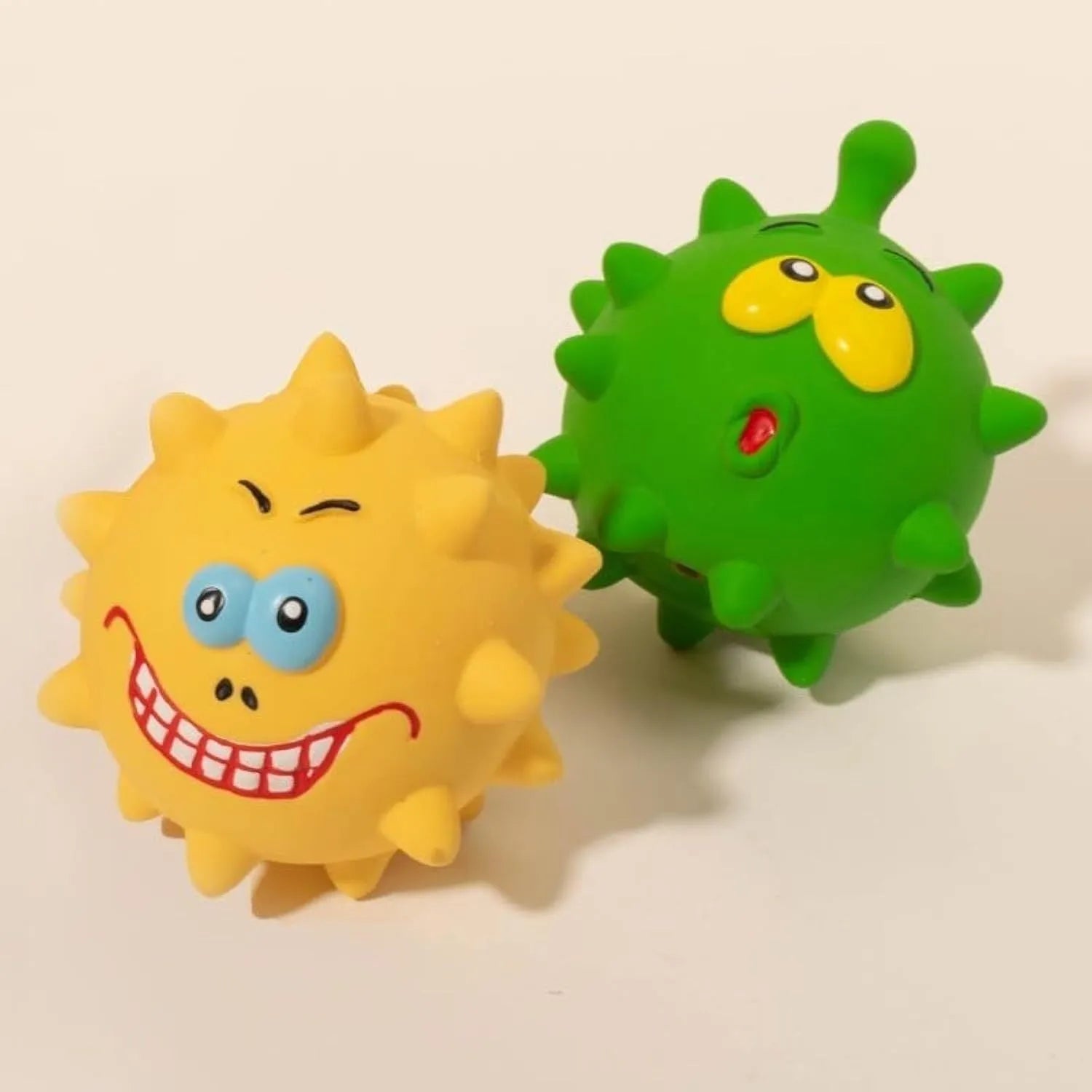 Set of four colourful latex squeaky dog balls with cute faces on a textured surface.