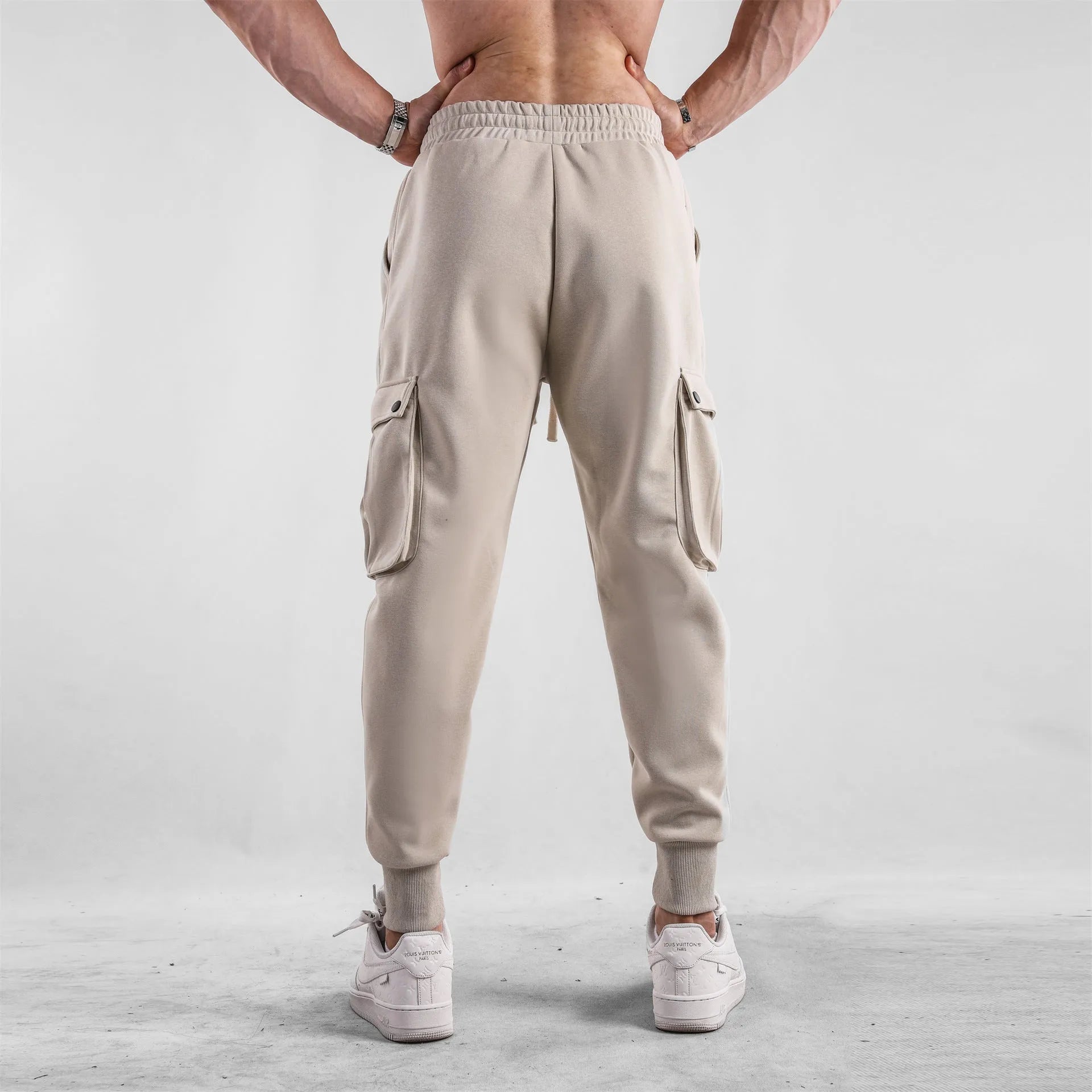 Men's loose-fit beige trousers with ankle ties and multiple pockets, laid flat.