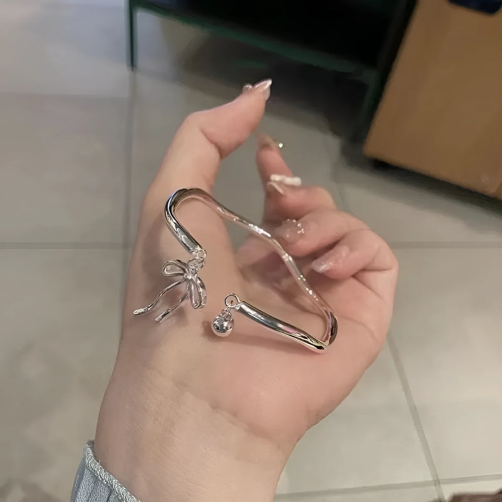 Silver adjustable bangle bracelet with a detailed bow charm and small bell on a wrist.