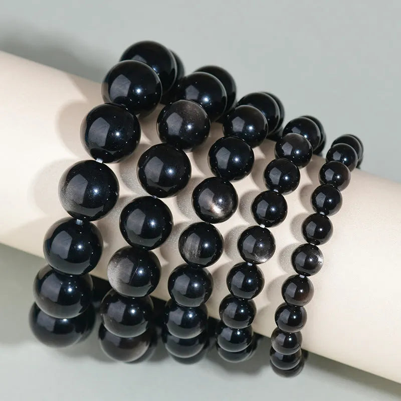 Hand-woven round obsidian crystal bracelet in black, silver, and rainbow eye colours on a neutral background.