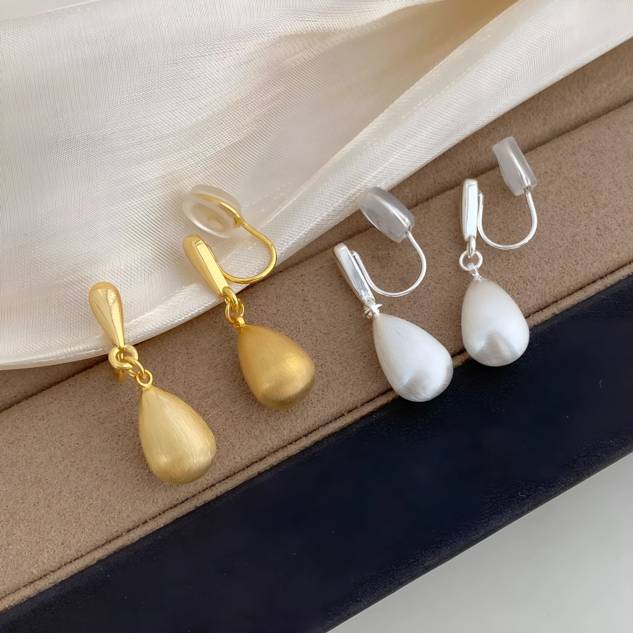 Close-up of wire drawing drop pendant ear clips in geometric teardrop shape, copper with gold electroplated finish