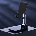 Folding telescopic mobile phone bracket in white, blue, green, or pink colours on a desktop.