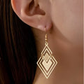Gold rhombus hollow stud earrings with diamond shape on a light background