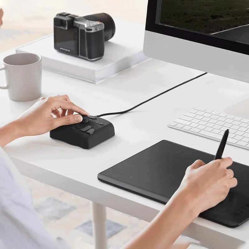 TourBox NEO video editing controller and auxiliary keyboard on a desk, showing its dials, buttons, and compact black design.