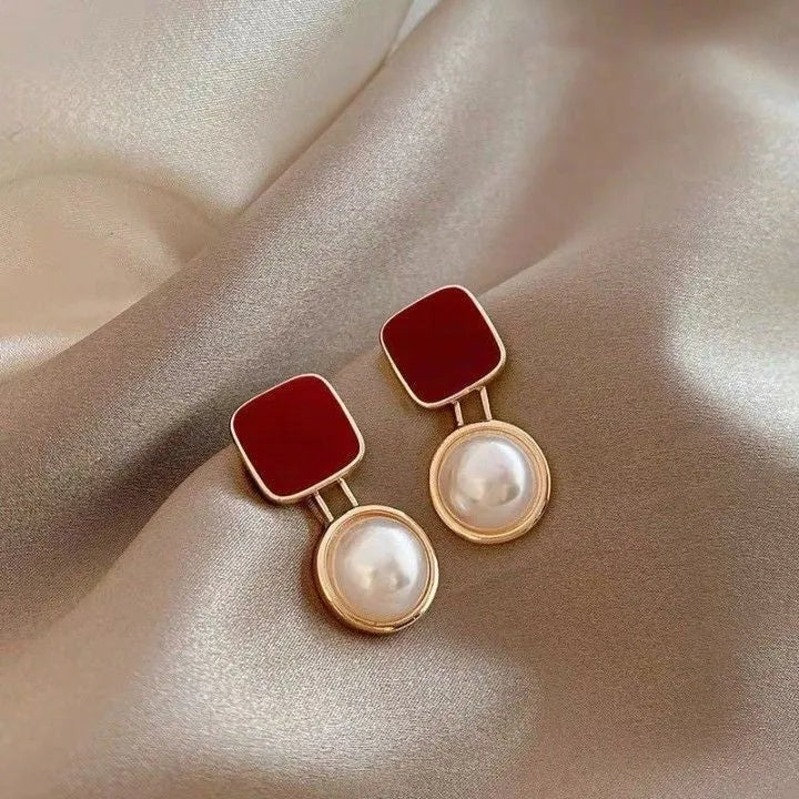 Red and blue geometric alloy stud earrings with pearl centre on neutral background