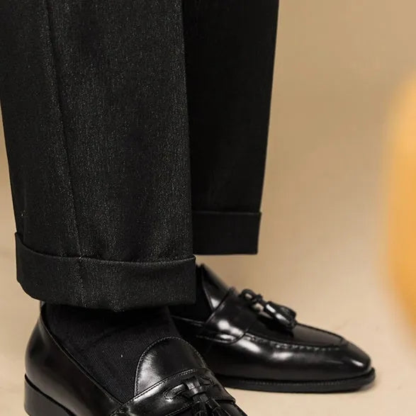Men's black polished leather tassel loafers with rubber sole, shown from the side.