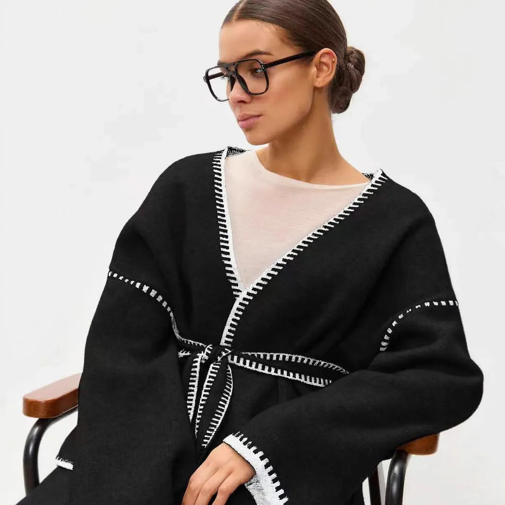 Loose beige knitted cardigan with a lace-up front, worn open over a white top.