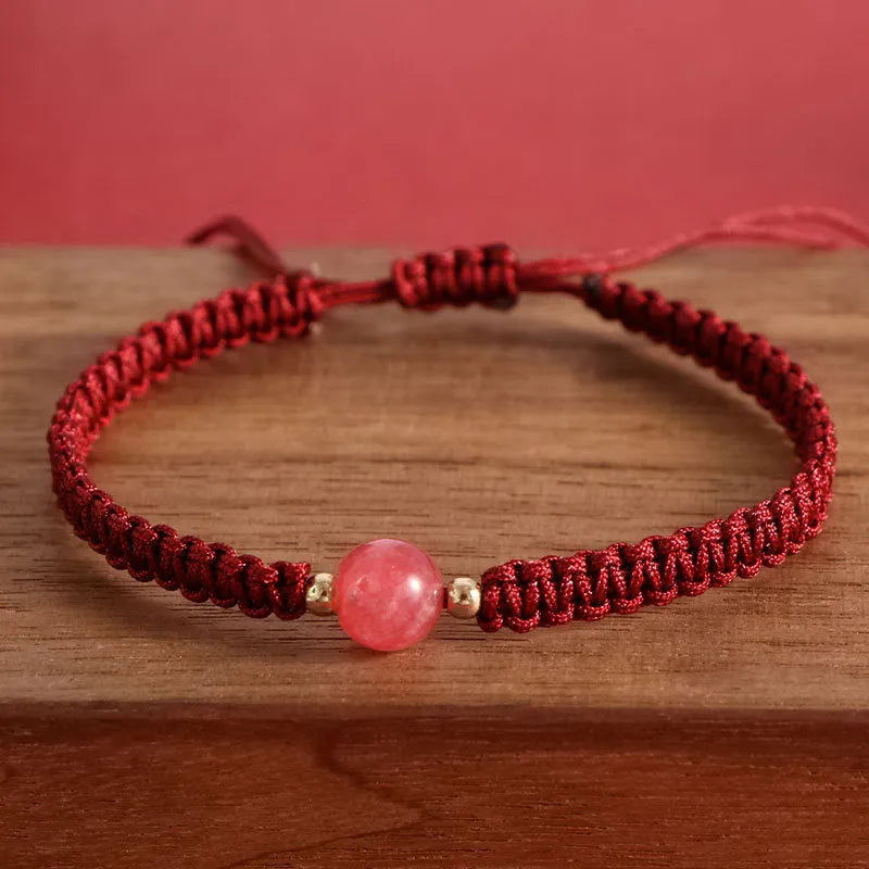A woven red rope bracelet with a natural strawberry quartz bead and an alloy clasp.