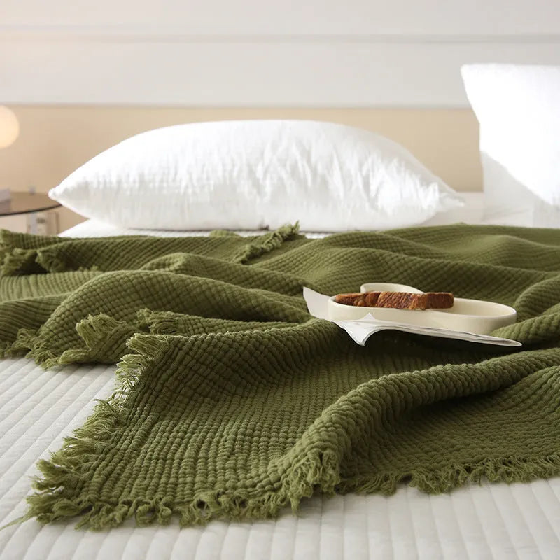 Cotton four-layer gauze blanket with tassel trim in avocado green colour, laid flat.