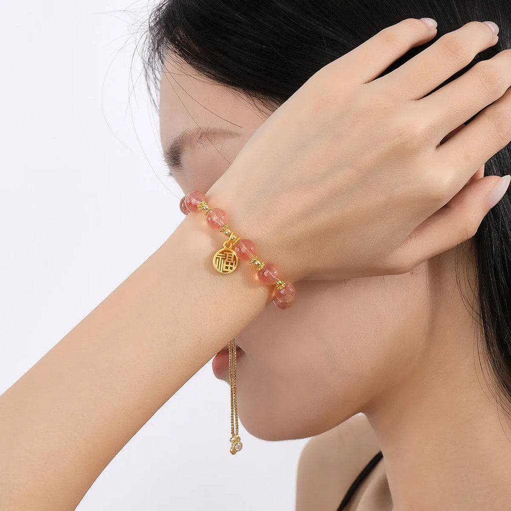 Women's strawberry quartz bracelet with geometric charms and fu character on wrist