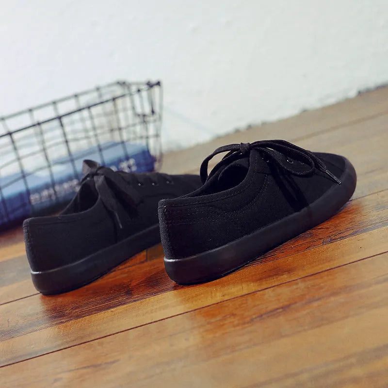 All black women's low-top canvas flat shoes with flat rubber sole and lace-up front.