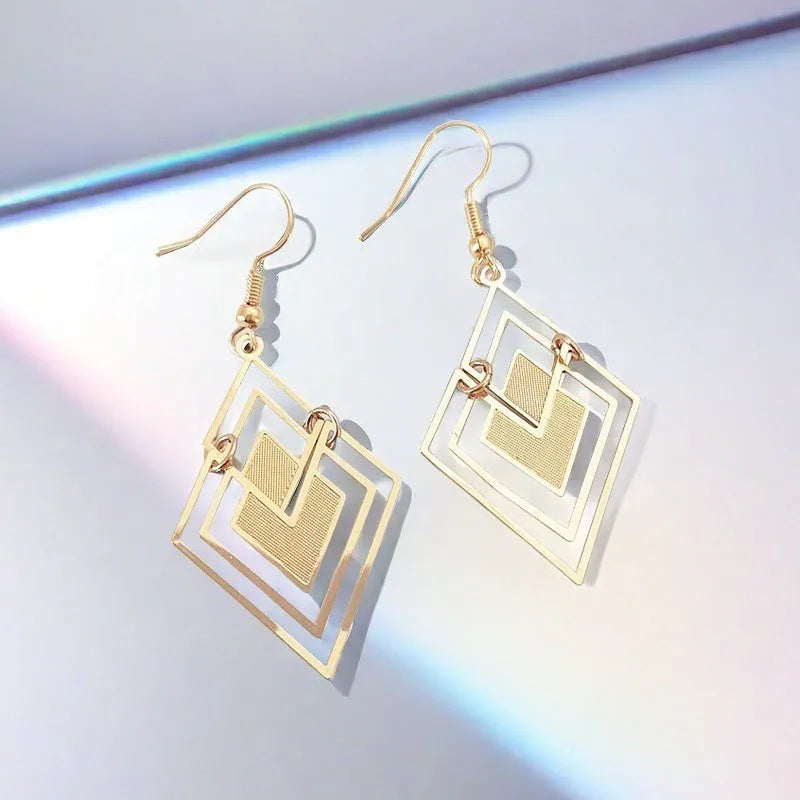 Gold rhombus hollow stud earrings with diamond shape on a light background