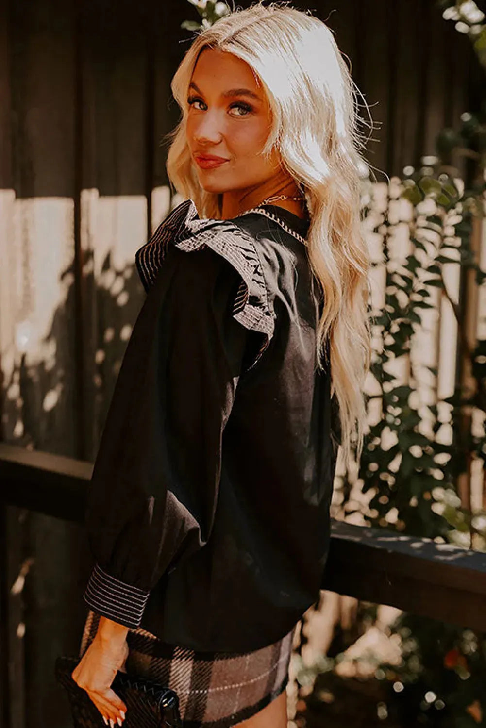 Black women's long-sleeve blouse with a V-neck, ruffle trim, and contrast stitching.