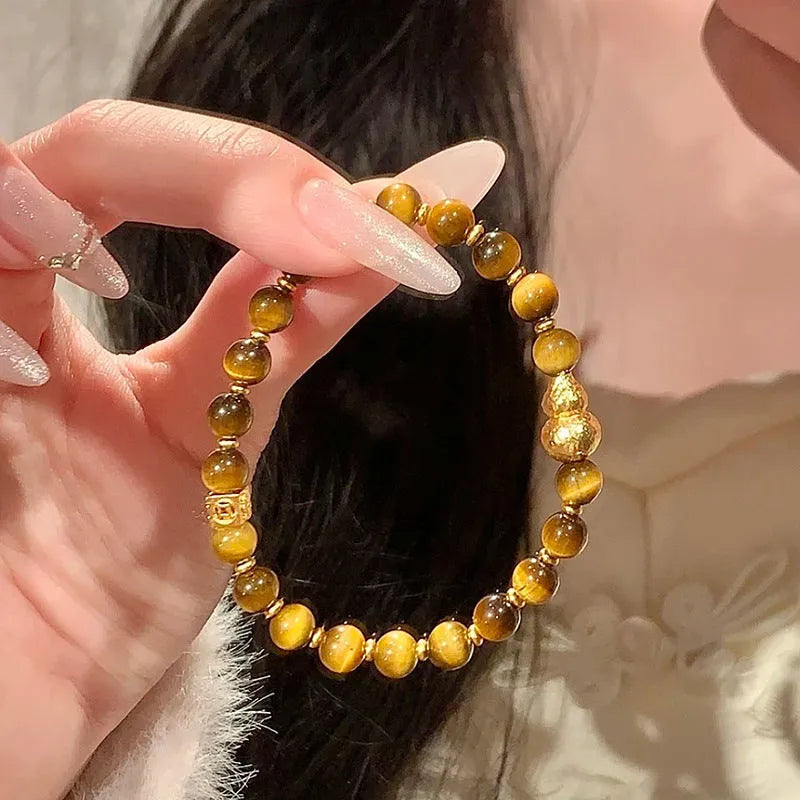 Natural yellow tiger's eye stone bracelet with gold gourd pattern on a white background.