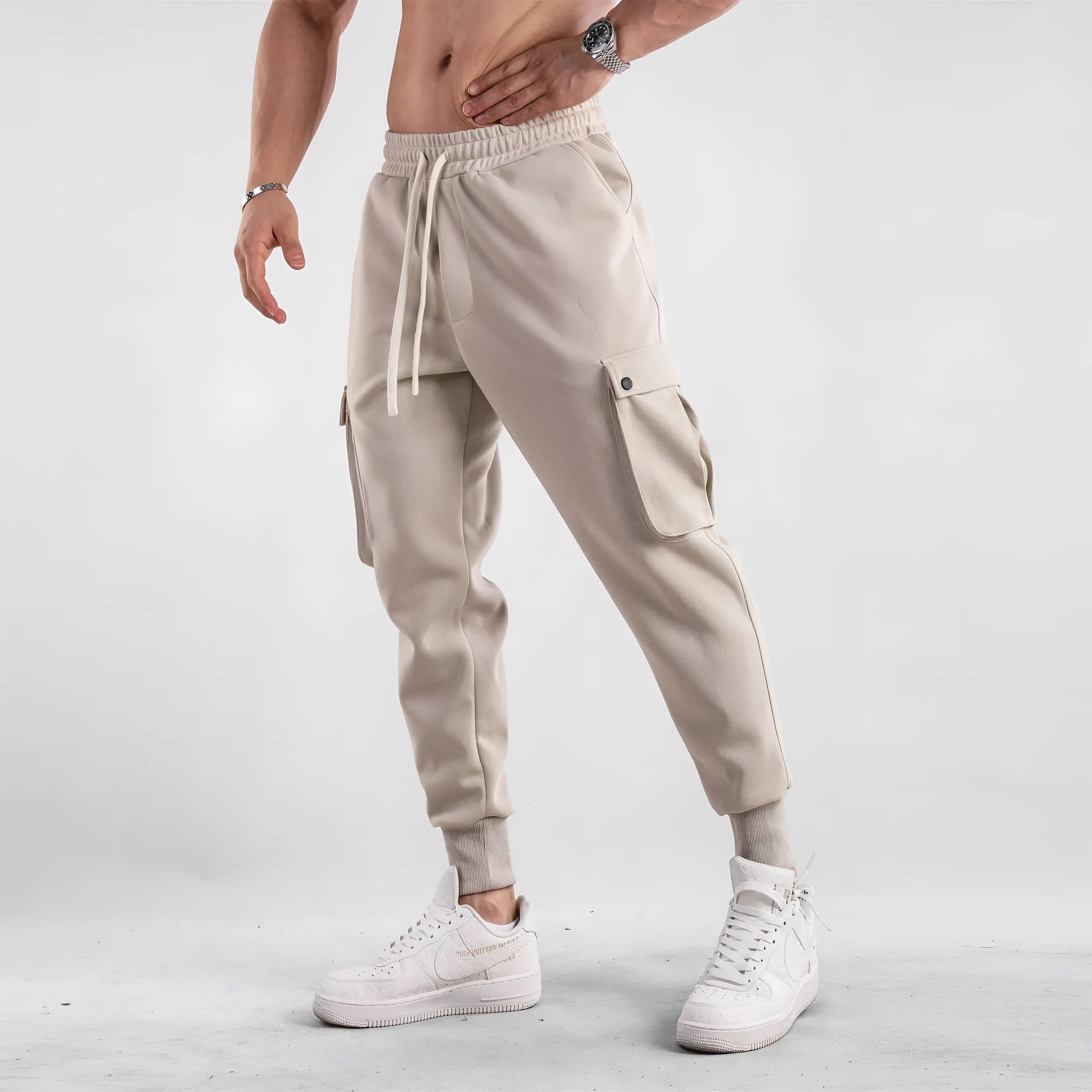Men's loose-fit beige trousers with ankle ties and multiple pockets, laid flat.