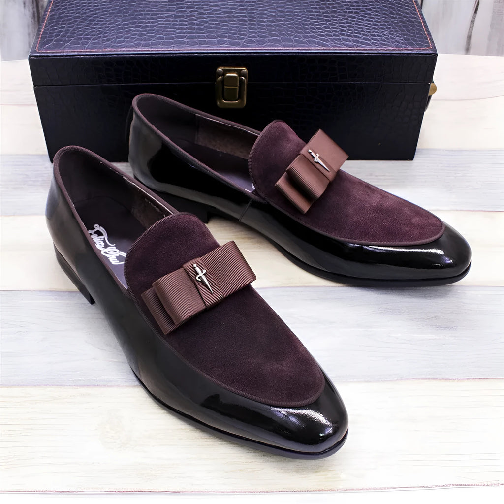 Men's glossy black patent leather tassel loafers with a low-top design and rubber sole on a wooden floor.