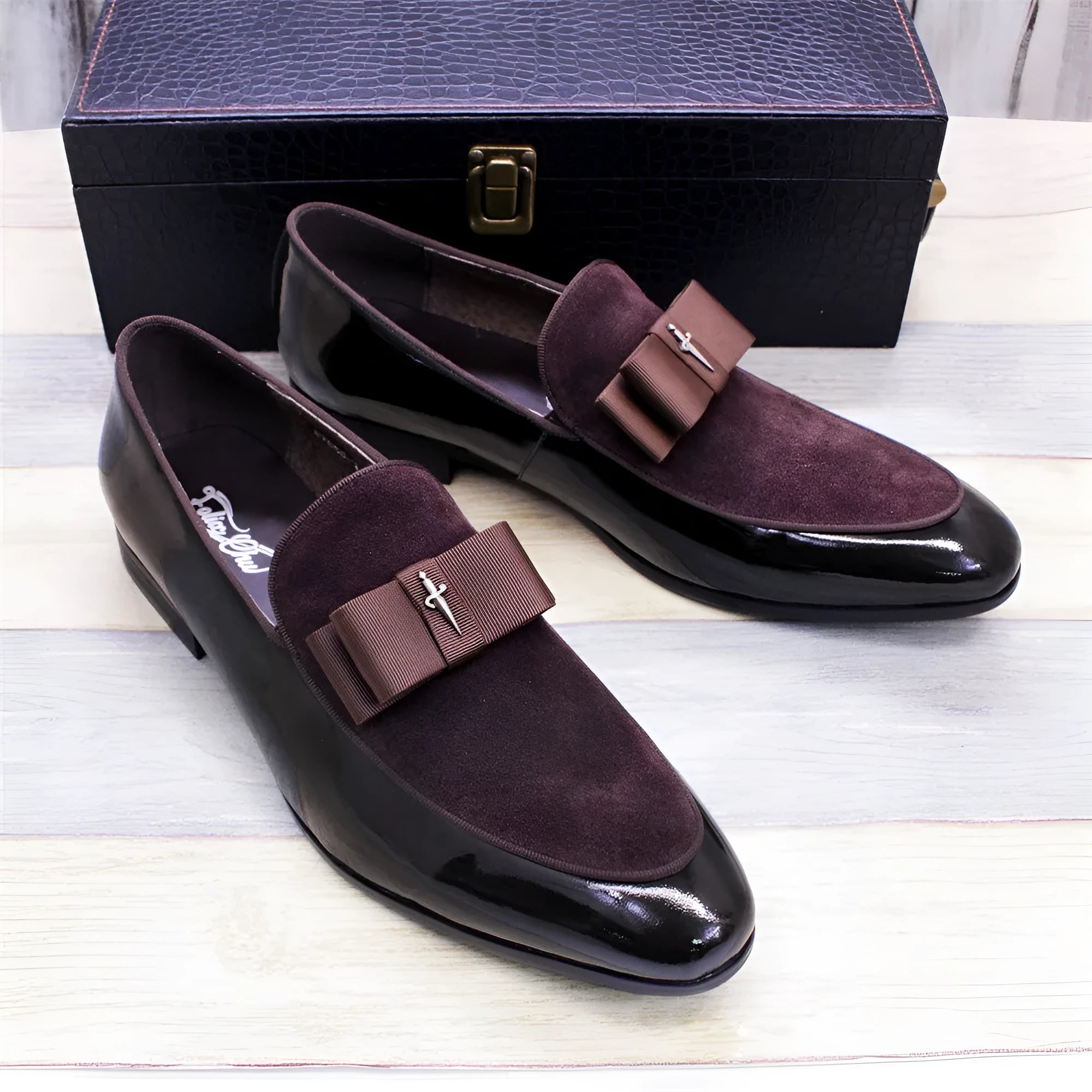 Men's glossy black patent leather tassel loafers with a low-top design and rubber sole on a wooden floor.