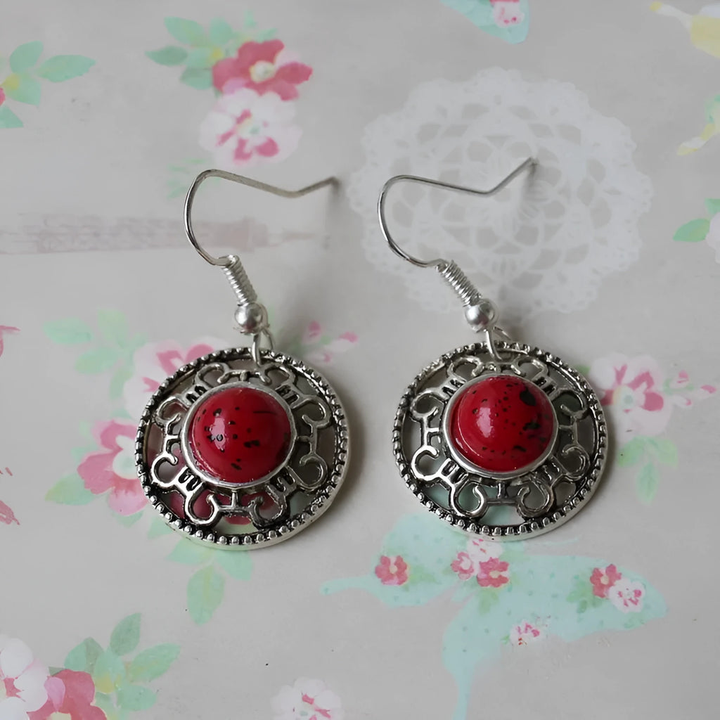 A pair of handmade ethnic earrings with a silver flower disc design, turquoise stones, and red decorative accents.