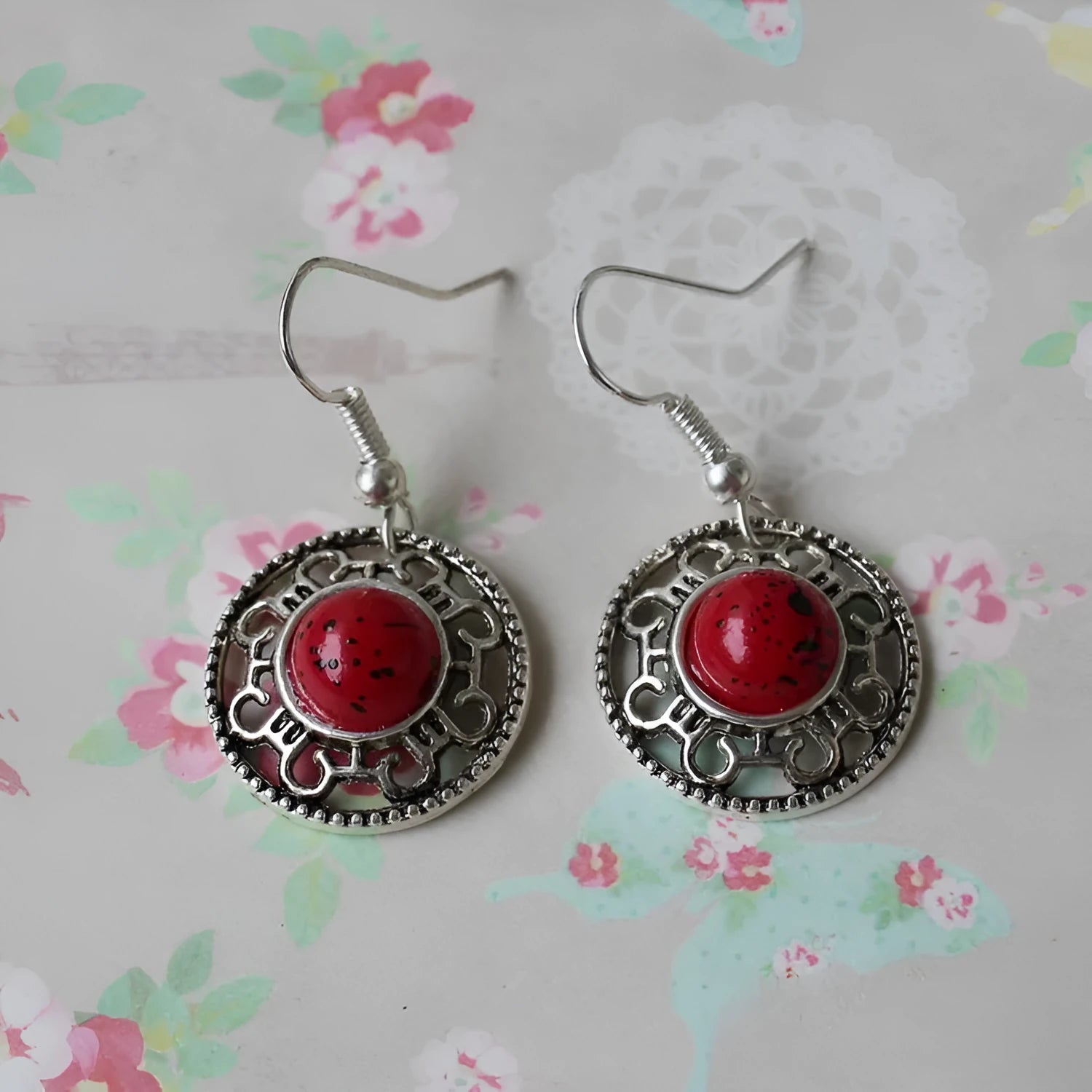 A pair of handmade ethnic earrings with a silver flower disc design, turquoise stones, and red decorative accents.