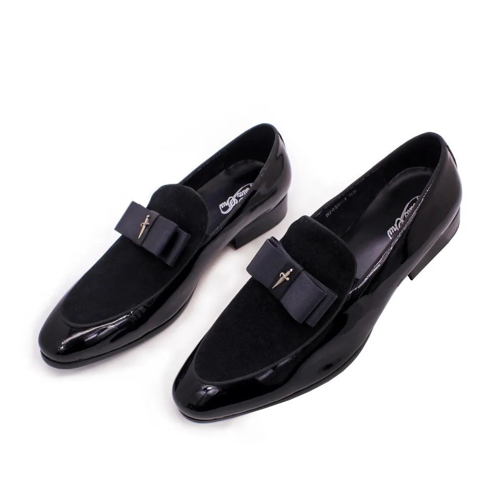 Men's glossy black patent leather tassel loafers with a low-top design and rubber sole on a wooden floor.