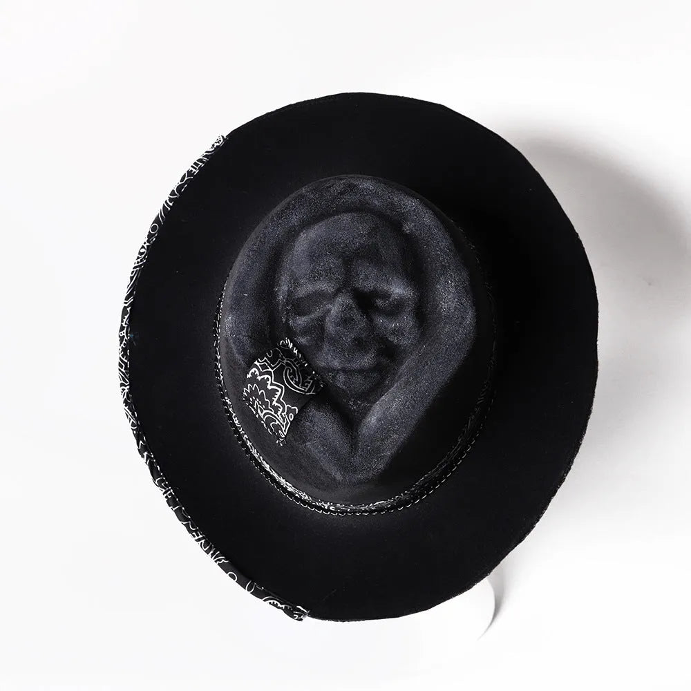 Handmade black wool felt skull hat with a pointed conical crown on a plain background.