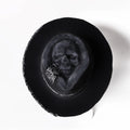 Handmade black wool felt skull hat with a pointed conical crown on a plain background.